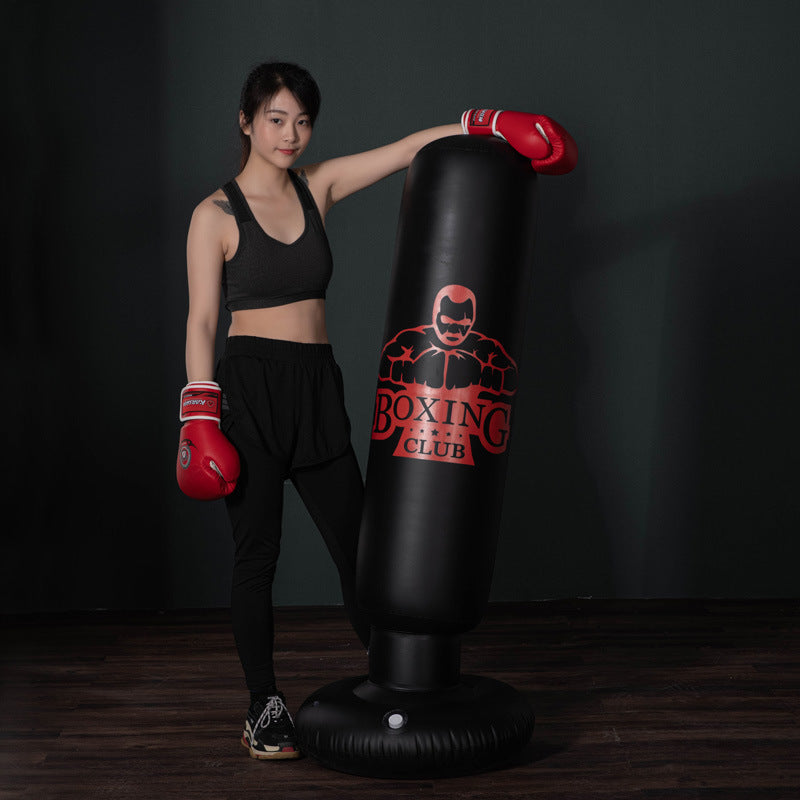 Woman standing next to a black free-standing kickboxing bag with red boxing gloves in a boxing gym