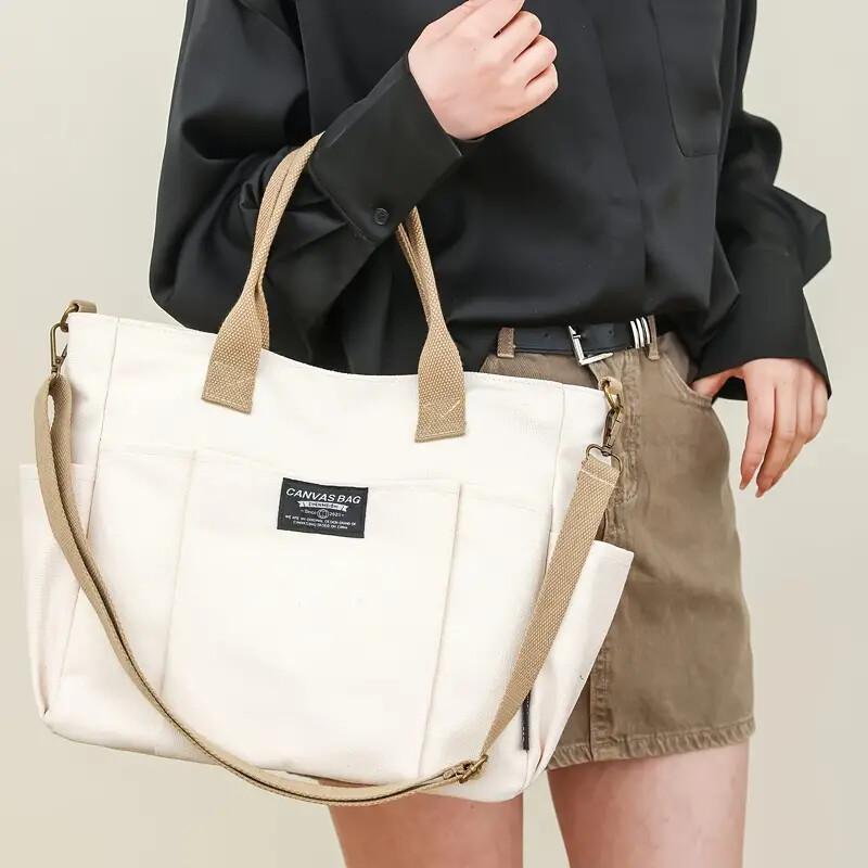 White multi pocket shoulder bag with beige straps worn by woman in black blouse and brown skirt