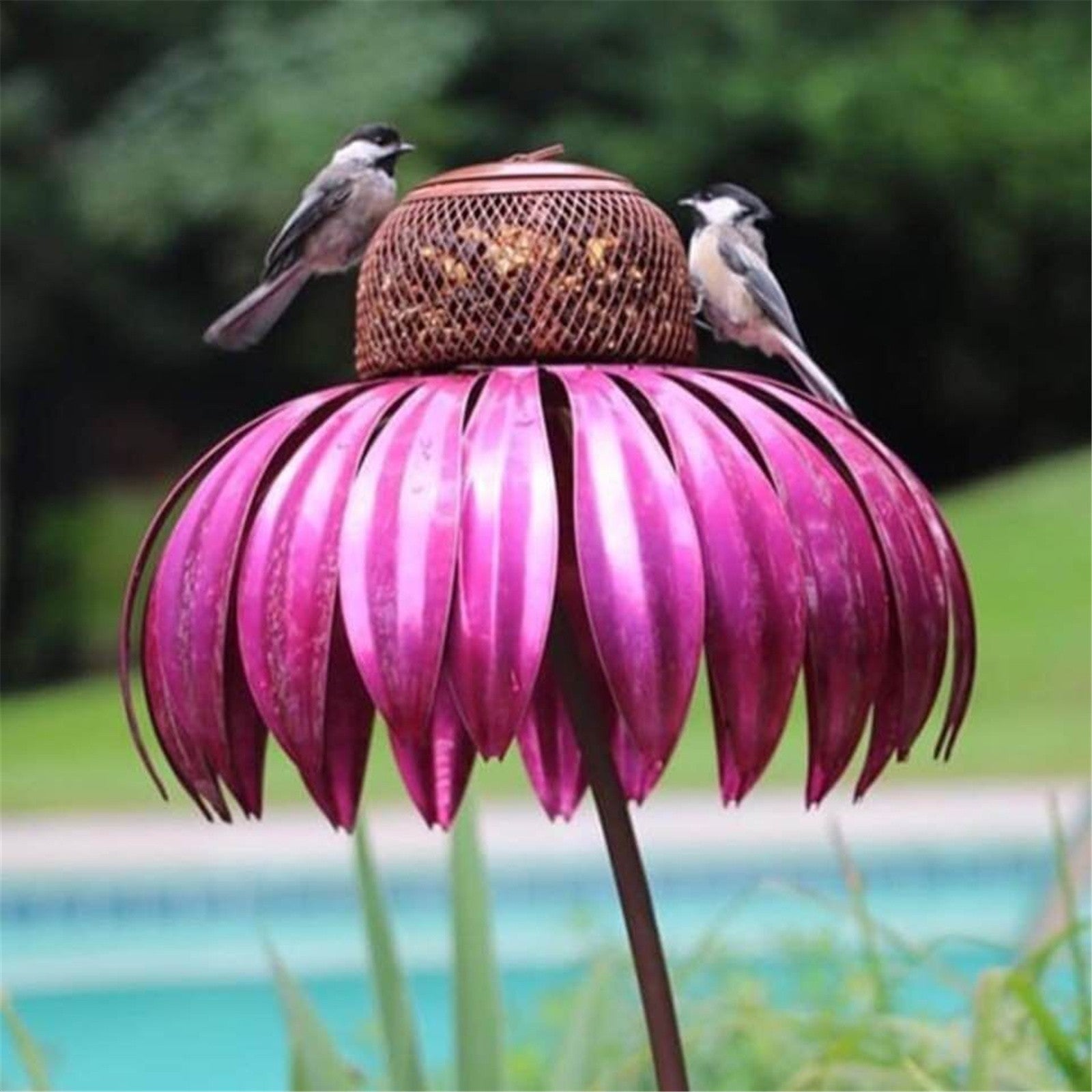 Petal shaped bird feeder in pink metal design with two small birds perched on top near a pool