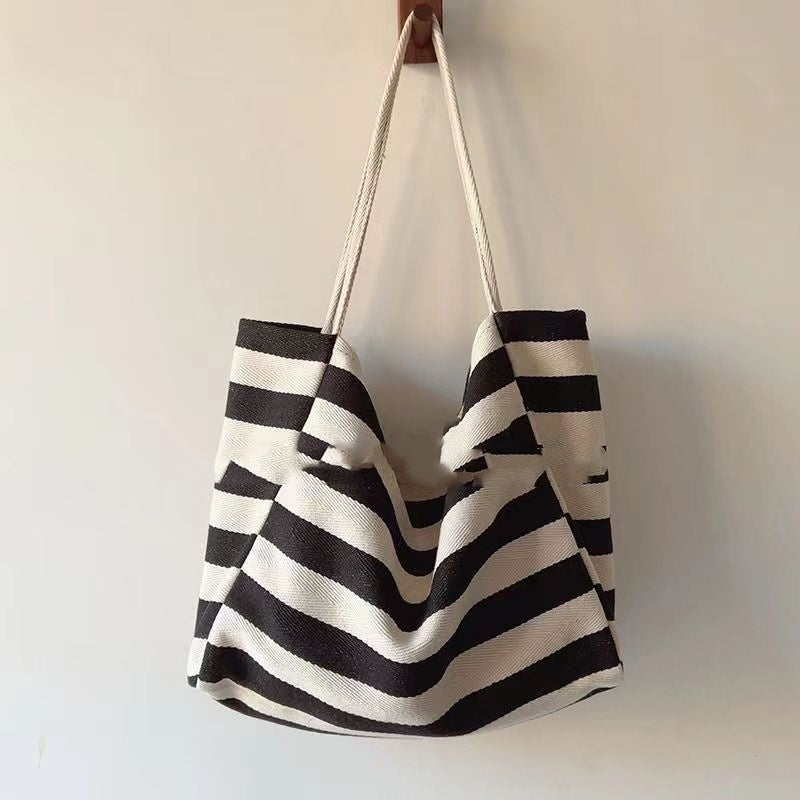 Striped canvas shoulder bag in black and white with long handles hanging on wall hook
