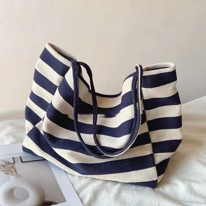 Striped canvas shoulder bag in navy and white with wide horizontal stripes and dual handles