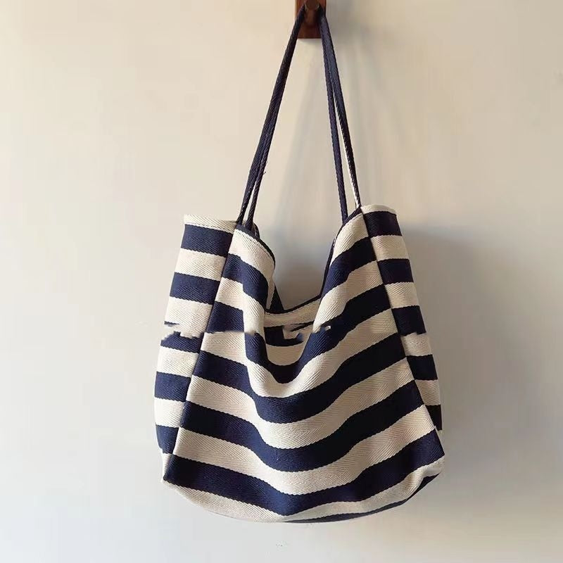 Striped canvas shoulder bag in navy and white with long handles hanging on wall