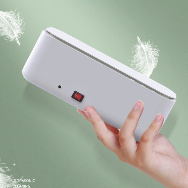 Hand holding white ultrasonic glasses cleaner with power switch on green background