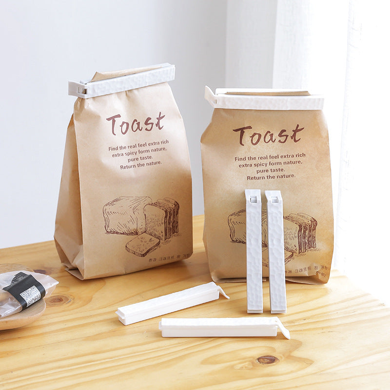 Reusable food sealing clips from Sheila Merchandise securing brown paper toast bags on wooden table