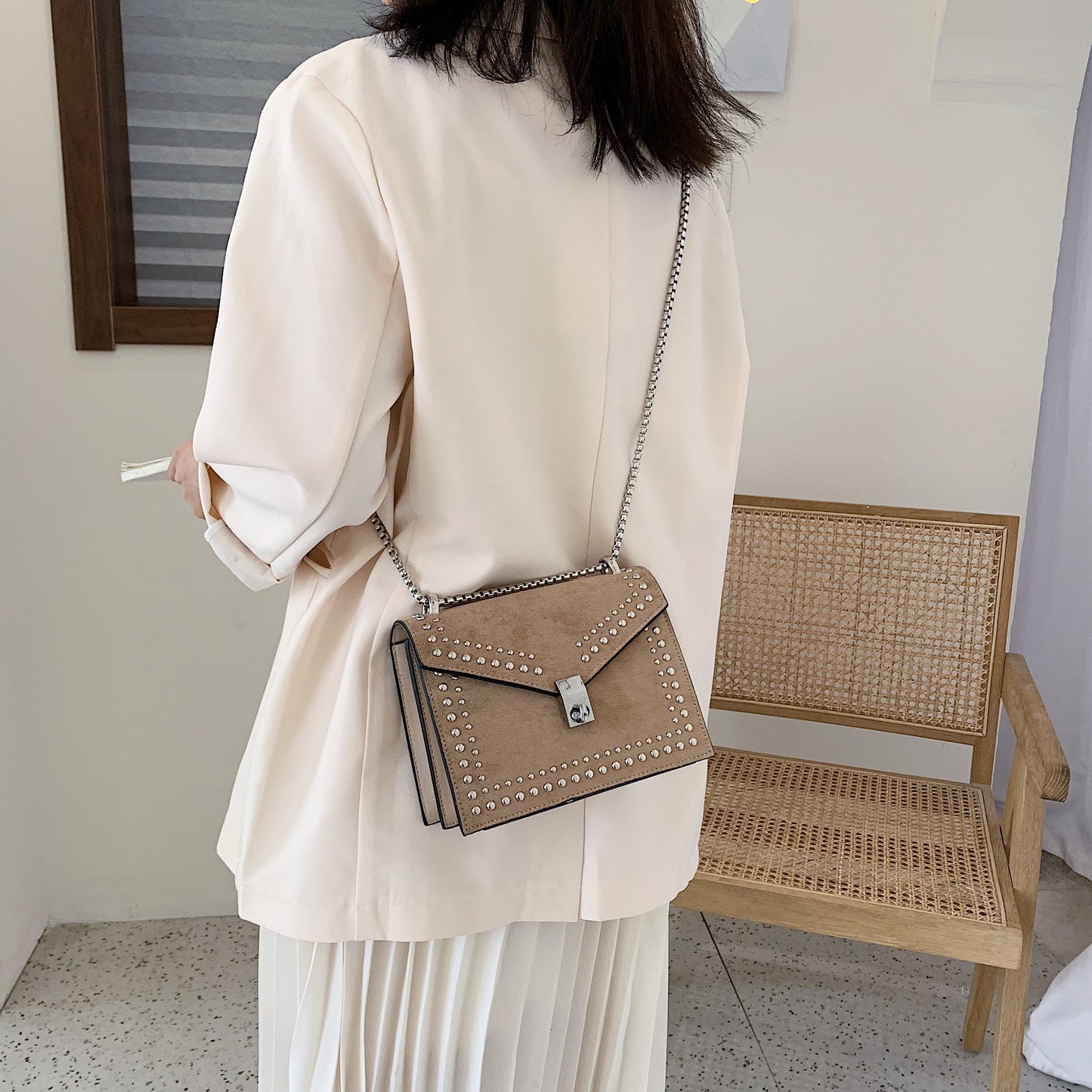 Beige studded purse with metal chain worn crossbody by woman in white outfit