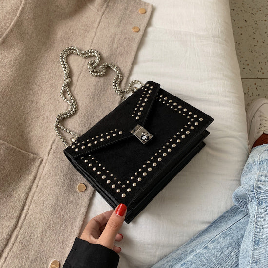 Black women's red leather purse with chain featuring silver studs and a silver clasp on a bed