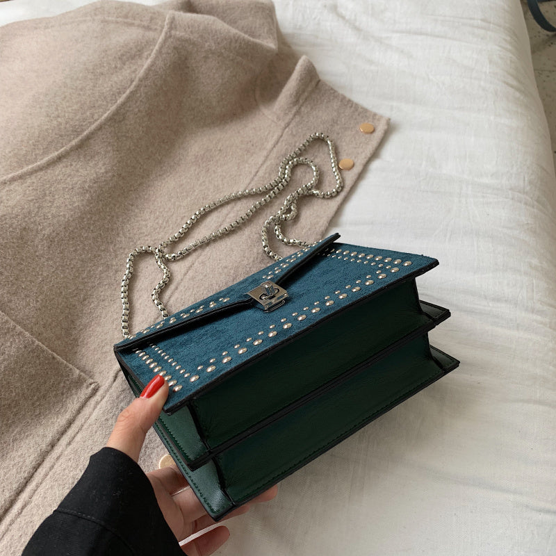 Women's red leather purse with chain held over beige coat on white bed