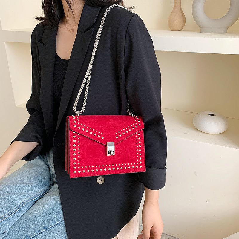 Women's red leather purse with chain strap and studded design worn with black blazer and jeans
