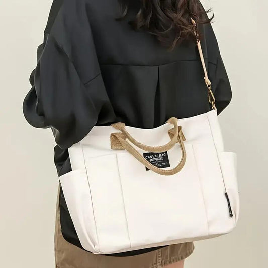 White multi pocket shoulder bag for women with canvas material and brown handles carried by a woman