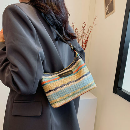 Simple stylish shoulder bag woven with multicolor stripes worn over shoulder by woman in gray blazer