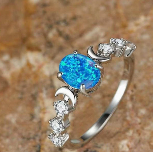 Moonstone love ring with bright blue center stone and crescent moon accents on silver band