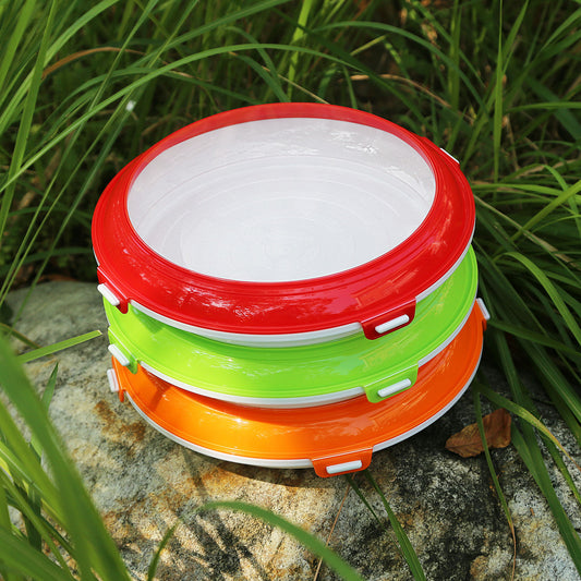 Stack of colorful food vacuum preservation trays with red, green, and orange lids placed outdoors on rock