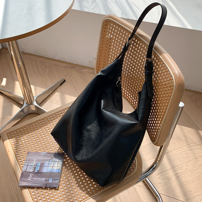 Black versatile leather shoulder bag by Sheila Merchandise on a woven chair in natural light
