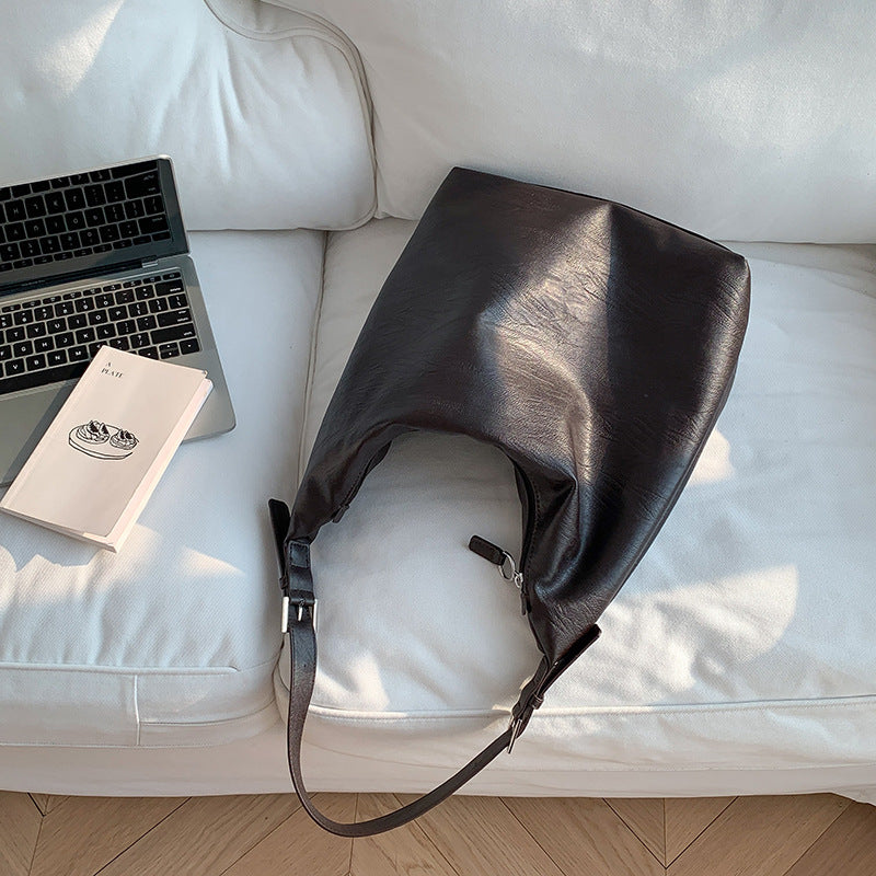 Black soft leather versatile leather shoulder bag placed on white couch next to laptop and book