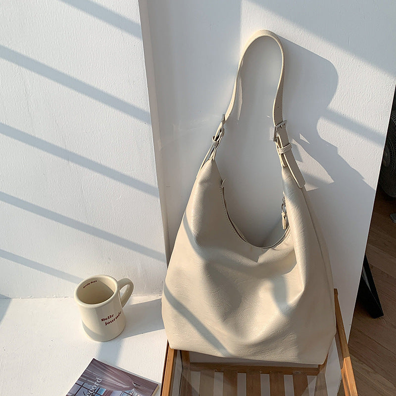 Versatile leather shoulder bag in soft cream leather hanging on white wall with sunlight exposure