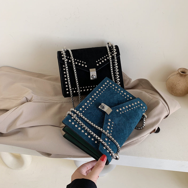 Hand holding women's red leather purse with chain in a room with other studded purses