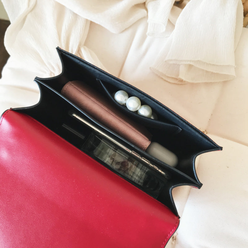 Open women's red leather purse with chain showing organized interior with wallet, pearls, and phone