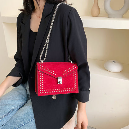 Women's red leather purse with chain strap and studded design worn with black blazer and jeans