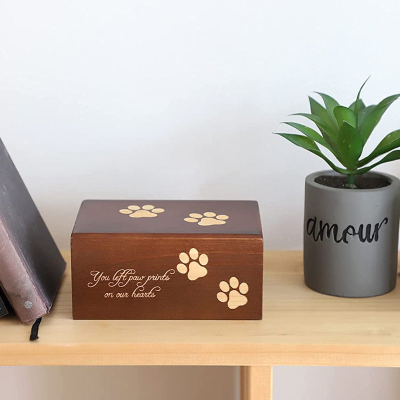 Wooden pet urn for ashes with paw print design and sentimental inscription on a wooden shelf